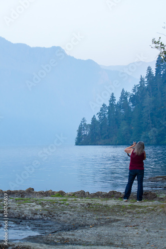 woman with camera shooting pictuers along the edge of mountain lake photo