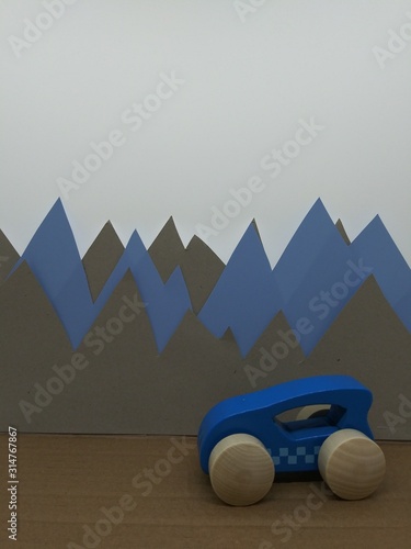 A blue toy car in front of an artistic mountain range