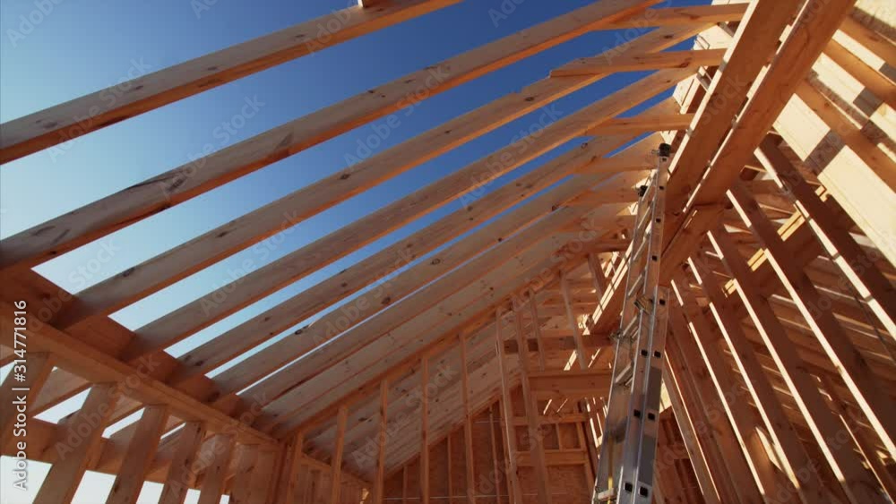 Sliding view from below of wooden beams of roof and walls of frame house under construction with blue sky on the background. Beautiful natural light, sunny day Sliding view from below of wooden beams of roof and walls of frame house under construction with blue sky on the background. Beautiful natural light, sunny day