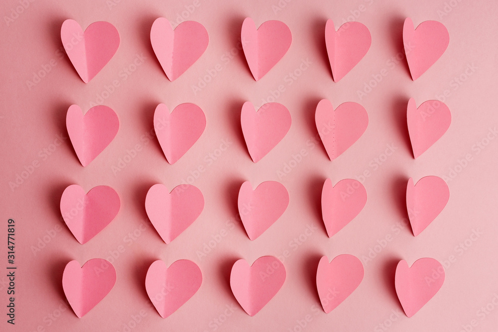 Pink paper hearts on pink background. Paper cut hearts arranged in rows on pink background. Flat lay. Top view