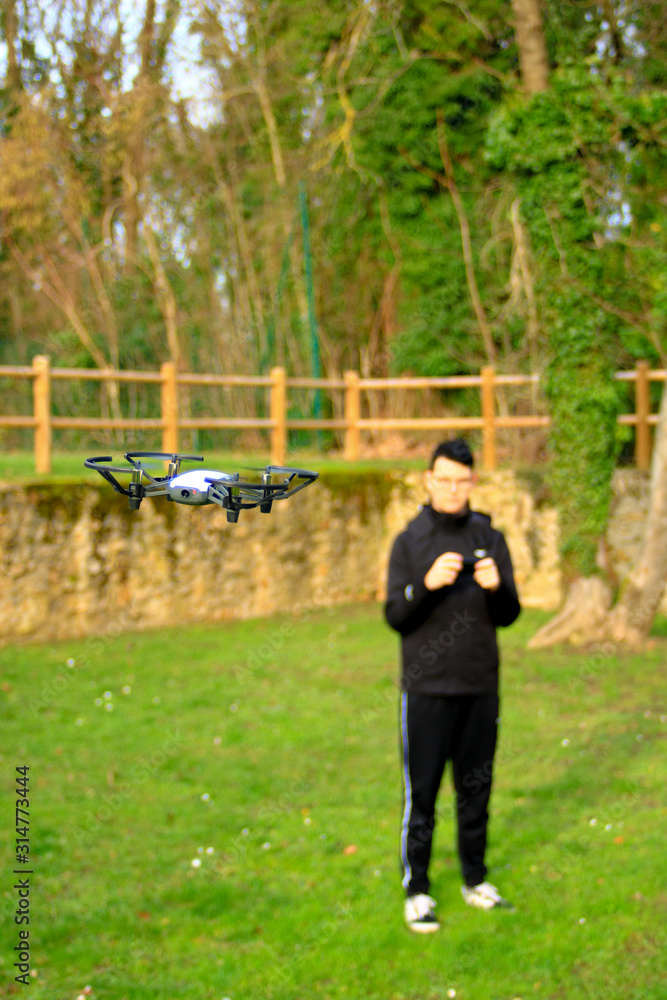 Small aircraft without crew. Teenage boy bokeh piloting a drone with his smartphone in a park outside. Small aircraft without crew. Teenage boy bokeh piloting a drone with his smartphone in a park outside.