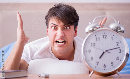 Man in bed frustrated suffering from insomnia with an alarm cloc photo