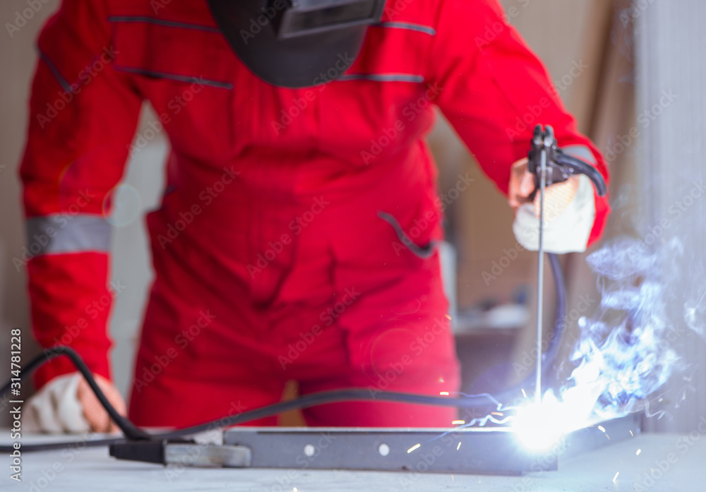 Obraz premium Young repairman with a welding gun electrode and a helmet weldin