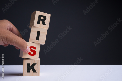 Financial risk assessment, risk reward and portfolio risk management concept. Four wood cubes stacked with  letters R, I, S, K on cubes. Hand trying to move a cube. Copy space.