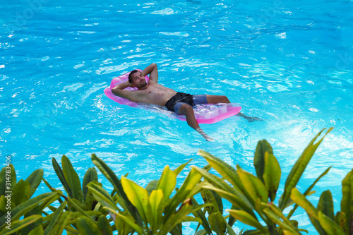 A man swims on a mattress in the pool. Relax in a hotel on a tropical island.