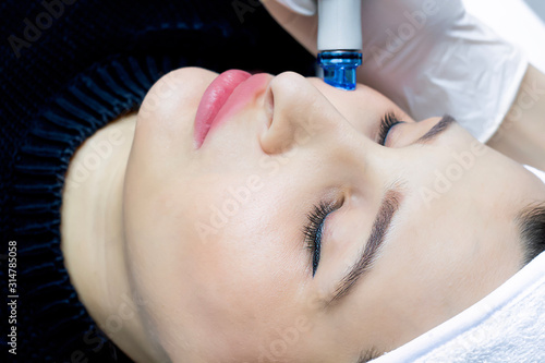Facial cleansing, vacuum hydro peeling. A young woman has a radiant face in a beauty salon, cosmetic facial skin care, a professional doctor, freshness and modern technology. Face massage