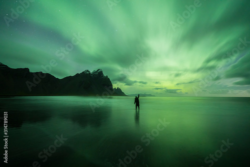 Aurora Borealis (Northern Lights) above a person at Stokksnes Beach and Vestrahorn Mountains, Iceland