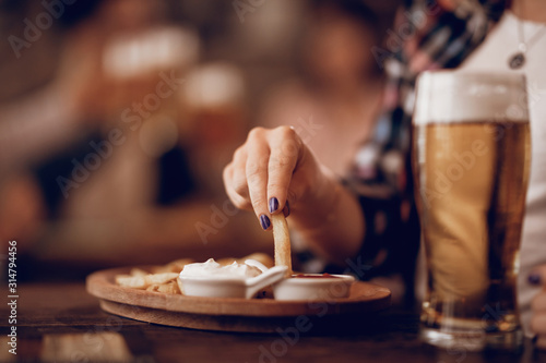 Close-up of woman eating French fries in a pub.
