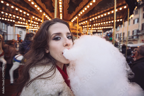 Portrait of a beautiful young girl with white cotton candy in front of a carousel horse