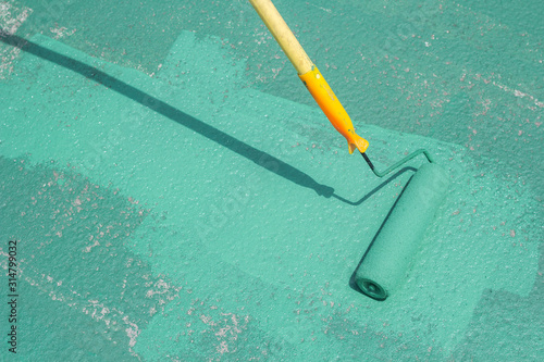 Hand painting a green floor with a paint roller for waterproofing