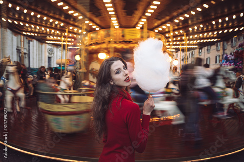 Portrait of a beautiful young girl with white cotton candy in front of a carousel horse