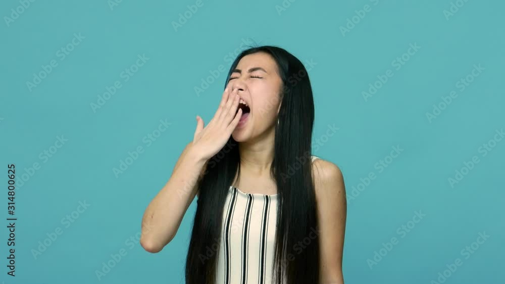 Sleepy overworked asian woman with long black hair yawning and covering mouth with hand, fatigued employee feeling drowsy and lazy, lack of energy. indoor studio shot isolated on blue background Sleepy overworked asian woman with long black hair yawning and covering mouth with hand, fatigued employee feeling drowsy and lazy, lack of energy. indoor studio shot isolated on blue background