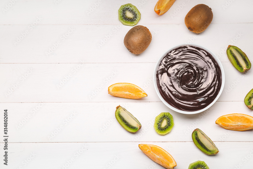 Bowl with tasty chocolate fondue and fruits on table - obrazy, fototapety, plakaty 