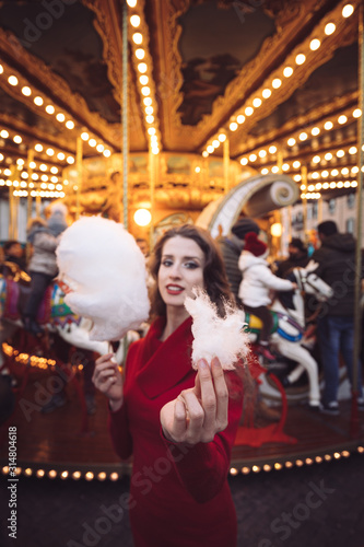 Portrait of a beautiful young girl with white cotton candy in front of a carousel horse