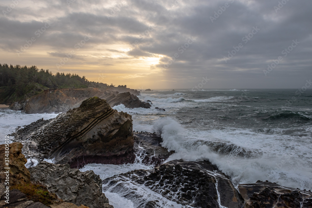 Fototapeta premium Sunset with stormy clouds and crashing waves at Shore Acres State Park, Charleston Oregon, USA