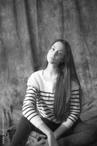Lovely young girl model with dark long hair in a striped sweater and skinny jeans posing in the studio on a textile background. Beauty and fashion. © capable97