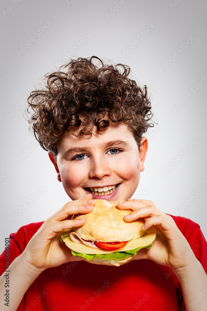 Boy eating big sandwich on gray background