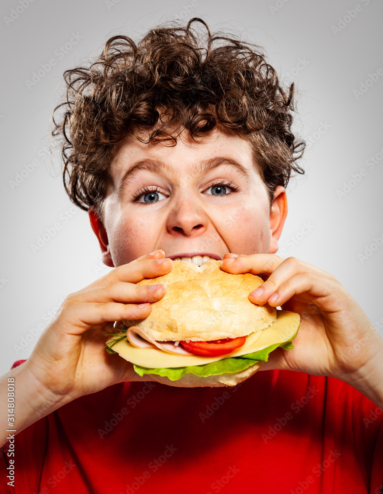 Boy eating big sandwich on gray background Boy eating big sandwich on gray background