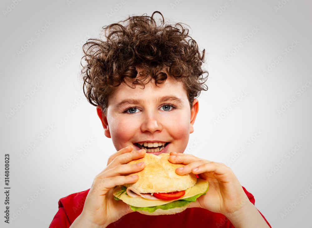 Fotografie Boy eating big sandwich on gray background