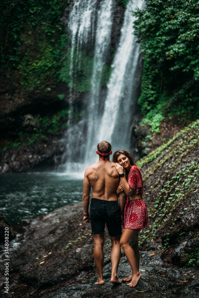 A beautiful girl embraces a man of athletic build at the waterfall. Honeymoon trip. A couple in love on a waterfall. Happy couple in Bali. Beautiful couple travels the world. Lonely couple in love A beautiful girl embraces a man of athletic build at the waterfall. Honeymoon trip. A couple in love on a waterfall. Happy couple in Bali. Beautiful couple travels the world. Lonely couple in love