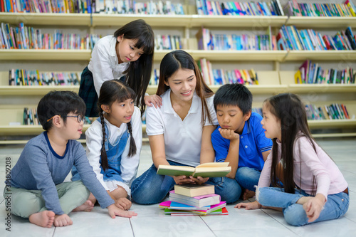 A Group of Asian Student Kid Reading a book with women teacher in School library with Shelf of Books in Background  Asian Kid Education Concept