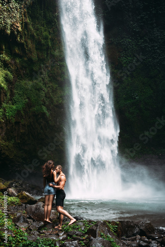A couple in love on a waterfall. A man of athletic build kisses a beautiful girl at the waterfall. Honeymoon trip. Declaration of love. Happy couple in Bali. Beautiful couple travels the world