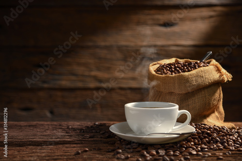 Cup of coffee with smoke and coffee beans on old wooden background