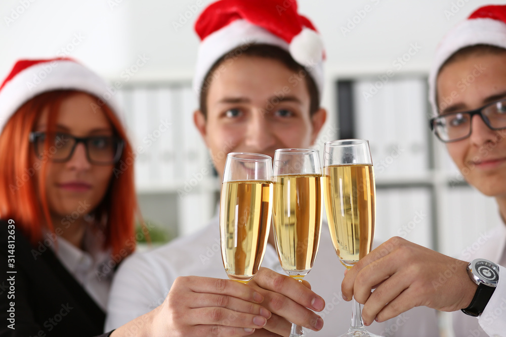A group of businesspeople celebrating Christmas New Year corporate in the office while toasting holding glasses of champagne in hands on their heads wearing Santa cap. A group of businesspeople celebrating Christmas New Year corporate in the office while toasting holding glasses of champagne in hands on their heads wearing Santa cap.