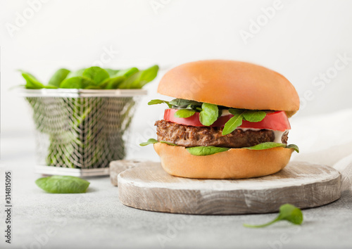 Healthy vegetarian meat free burger on round chopping board with vegetables and spinach on light table background. photo