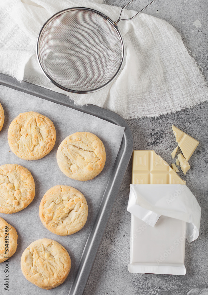White chocolate biscuit cookies on baking tray on light kitchen table background with white chocolate bar. White chocolate biscuit cookies on baking tray on light kitchen table background with white chocolate bar.