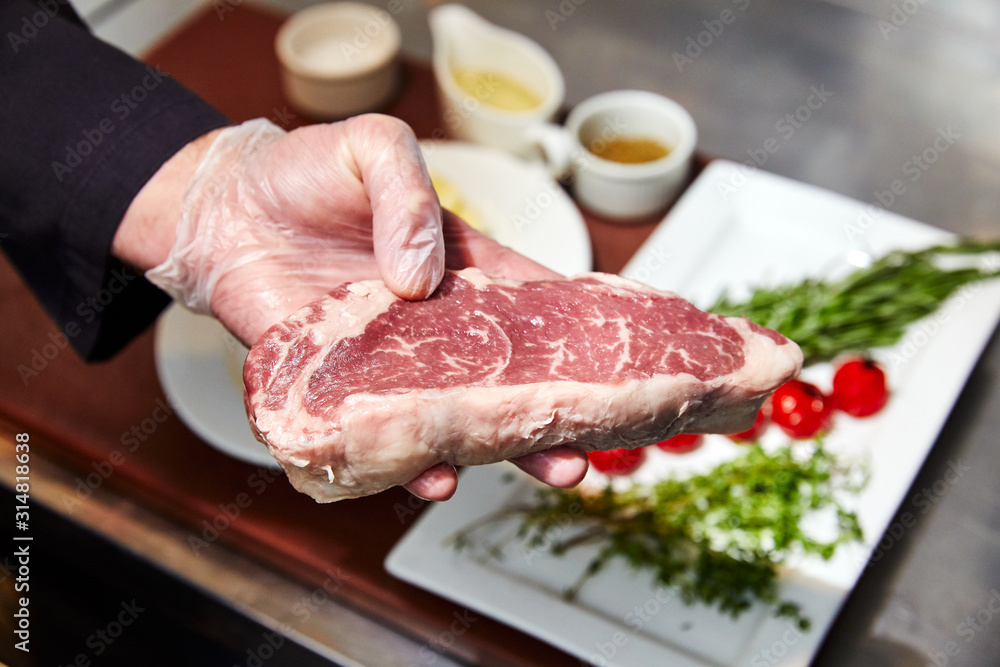 raw piece of meat in the palm of a person, preparing to cook, against the background of vegetables