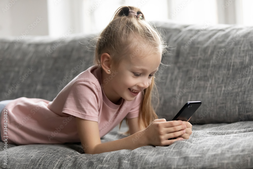 Smiling little girl lying on sofa using smartphone Smiling little girl lying on sofa using smartphone