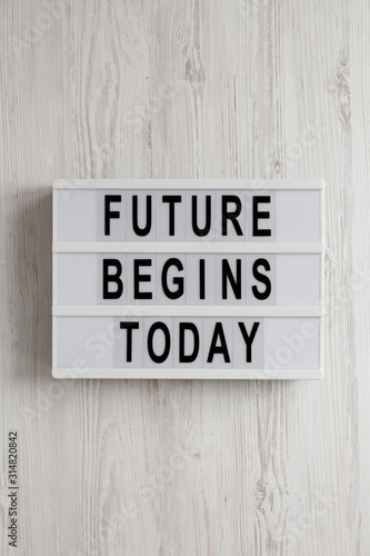 'Future begins today' words on a lightbox on a white wooden background, top view. Overhead, from above, flat lay.