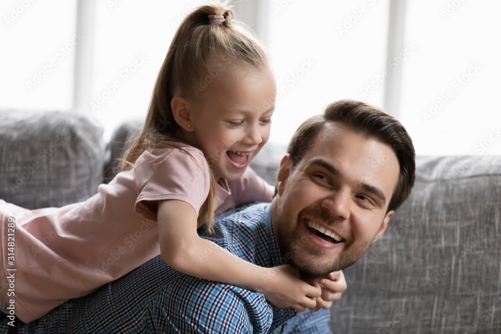 Fototapeta premium Overjoyed dad playing with excited cute little daughter at home