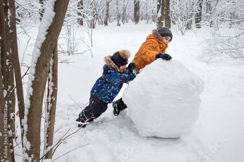 Canvas Print boys ride a big snowball in a winter forest