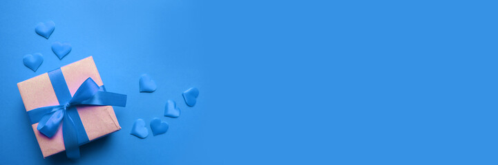 Top view minimalistic composition with surprise gift box and silk ribbon bow and heart shape on blue background.