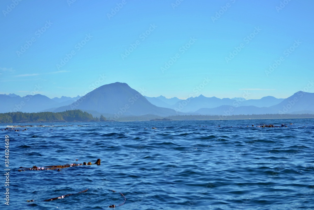 Pacific ocean with silhouettes of misty mountains in the background. Dark blue water, light blue sky, sunny day.