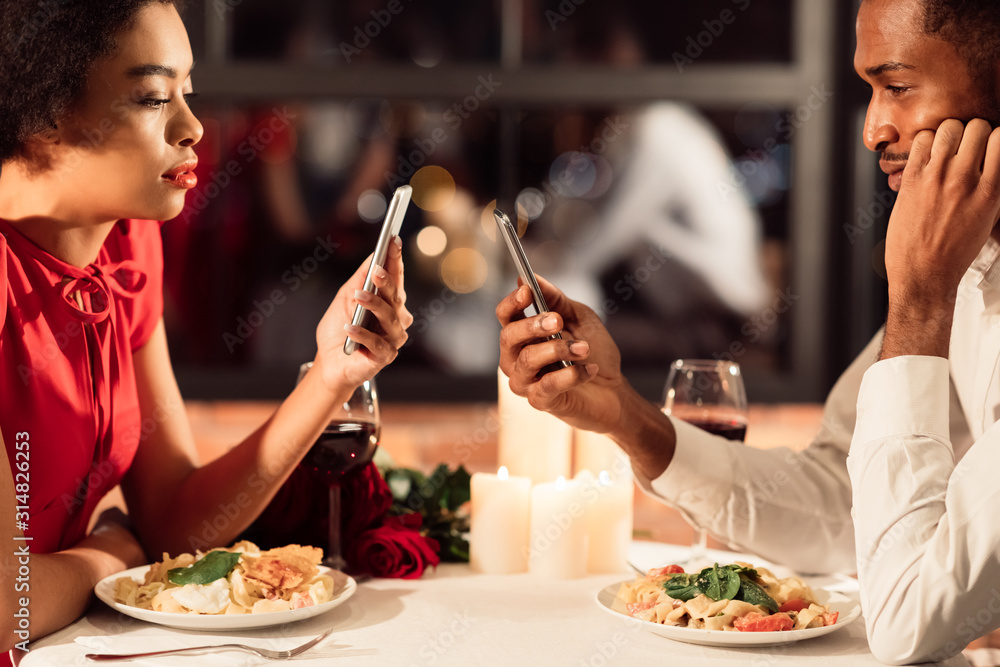 Bored African American Couple Using Phones During Date In Restaurant - obrazy, fototapety, plakaty 