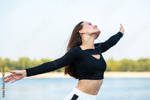 Charming brunette girl smiling and enjoying life outdoor. Young woman. Female model posing over nature background with river  beach and blue clean sky. Freedom  youth lifestyle  active leisure