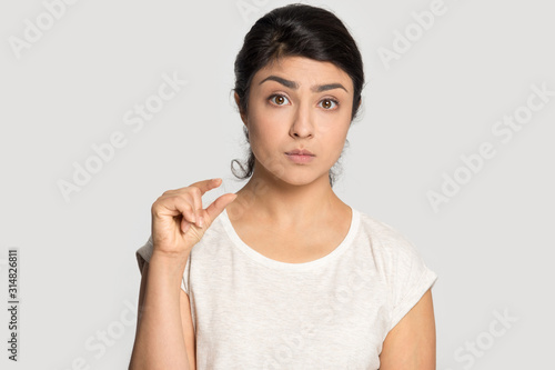 Frustrated millennial indian ethnicity woman demonstrating tiny measurement.
