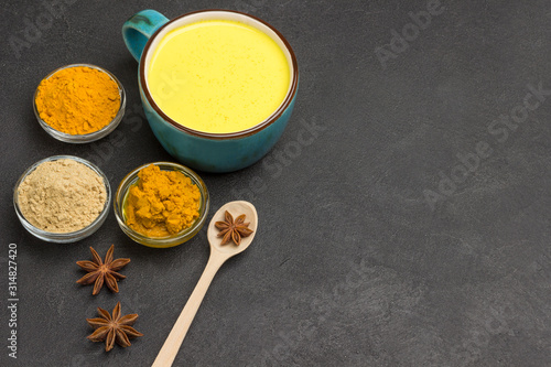 Golden latte with ingredients for cooking cardamom, cinnamon sticks, star anise on black background. Indian drink turmeric golden milk.