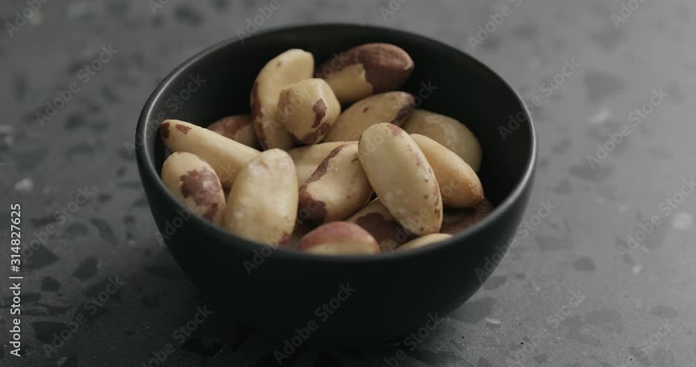 Slow motion man hand takes brazil nuts from black bowl on terrazzo countertop Slow motion man hand takes brazil nuts from black bowl on terrazzo countertop