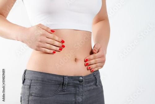 a young woman massages her stomach with two hands. on white