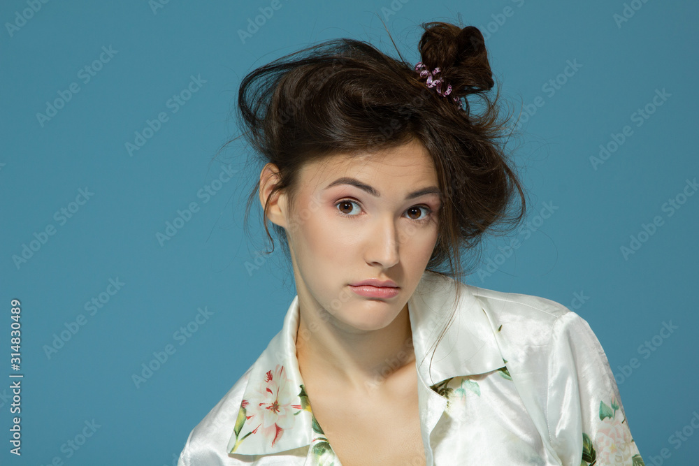 Portrait of cute morning girl. Beautiful cheerful teen girl looking at camera over blue background. Young woman posing in pajamas at studio.