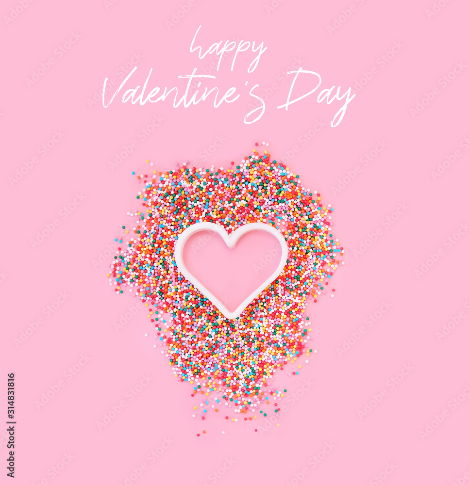 Happy Valentine's day greetings card. colored sugar grains and heart on pink background. love concept, minimal creative design. close up. flat lay.