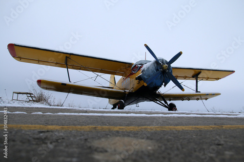 Fototapeta Naklejka Na Ścianę i Meble -  A picture from the airfield during the winter. The old biplane is standing on the runway and waiting for better weather, so it can fly again. 
