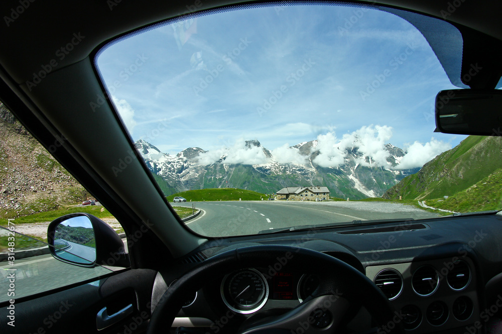 A view on the Alps through the windscreen of the car while driving on the curvy road. A view on the Alps through the windscreen of the car while driving on the curvy road.