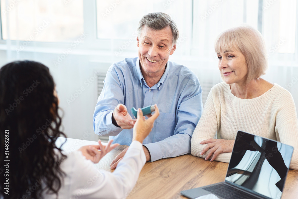 Obraz premium Female physician giving asthma inhaler to elderly couple