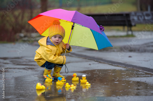 Obraz na plátně Beautiful funny blonde toddler boy with rubber ducks and colorful umbrella, jump