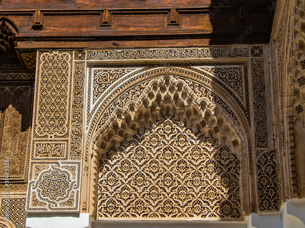 Detail of islamic building. It is an old architecture in the middle of the Moroccan city. There are white walls with wooden carved characters. There is summer time.